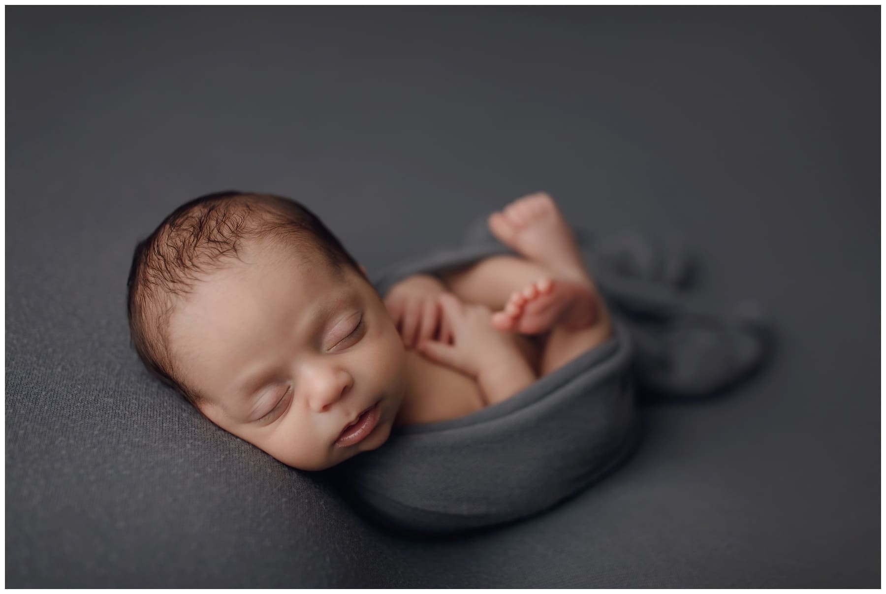 Newborn baby boy swaddled in dark grey wrap during newborn photo session with 8.08 Phtoography in Jacksonville Fl