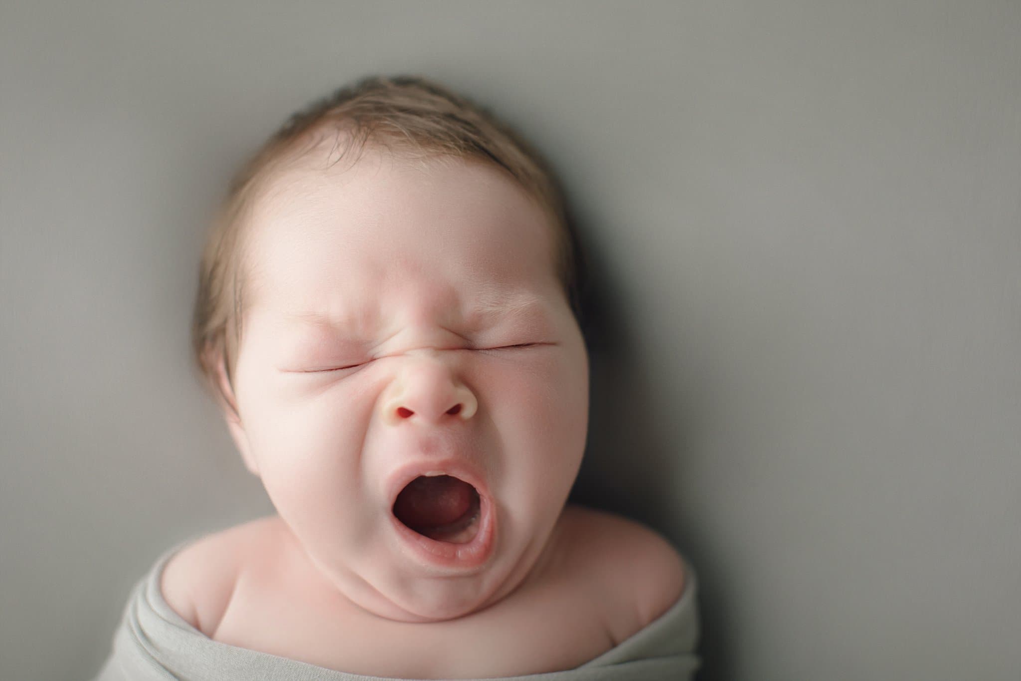 new baby photos yawning baby boy with a head full of hair on sage background