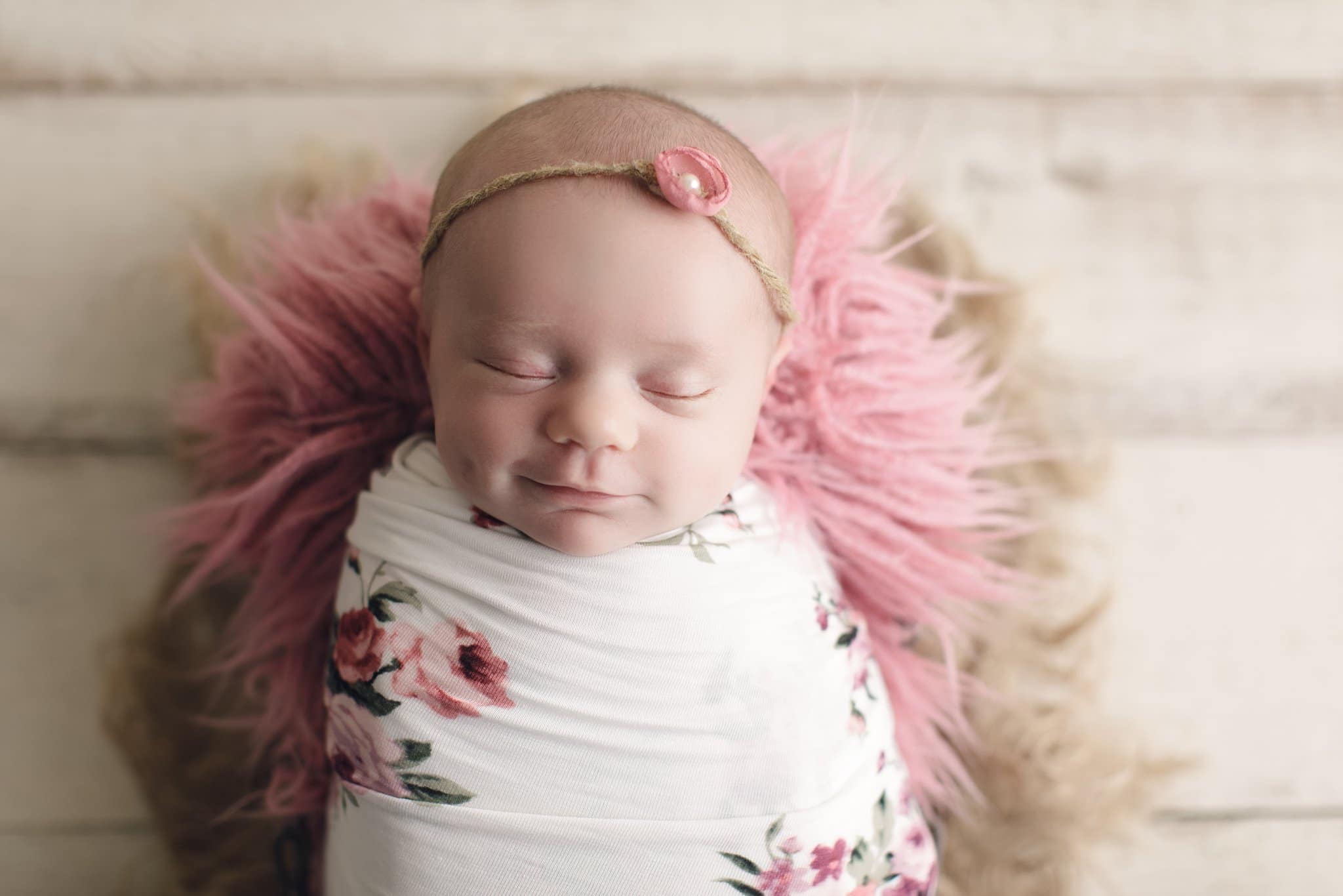 baby photography newborn baby girl swaddled in floral wrap and sleeping on dark pink fur