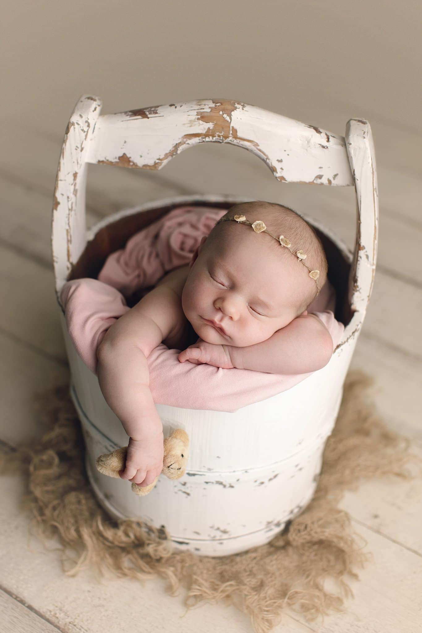newborn baby girl sleeping in water bucket holding teddy bear with arm dangling