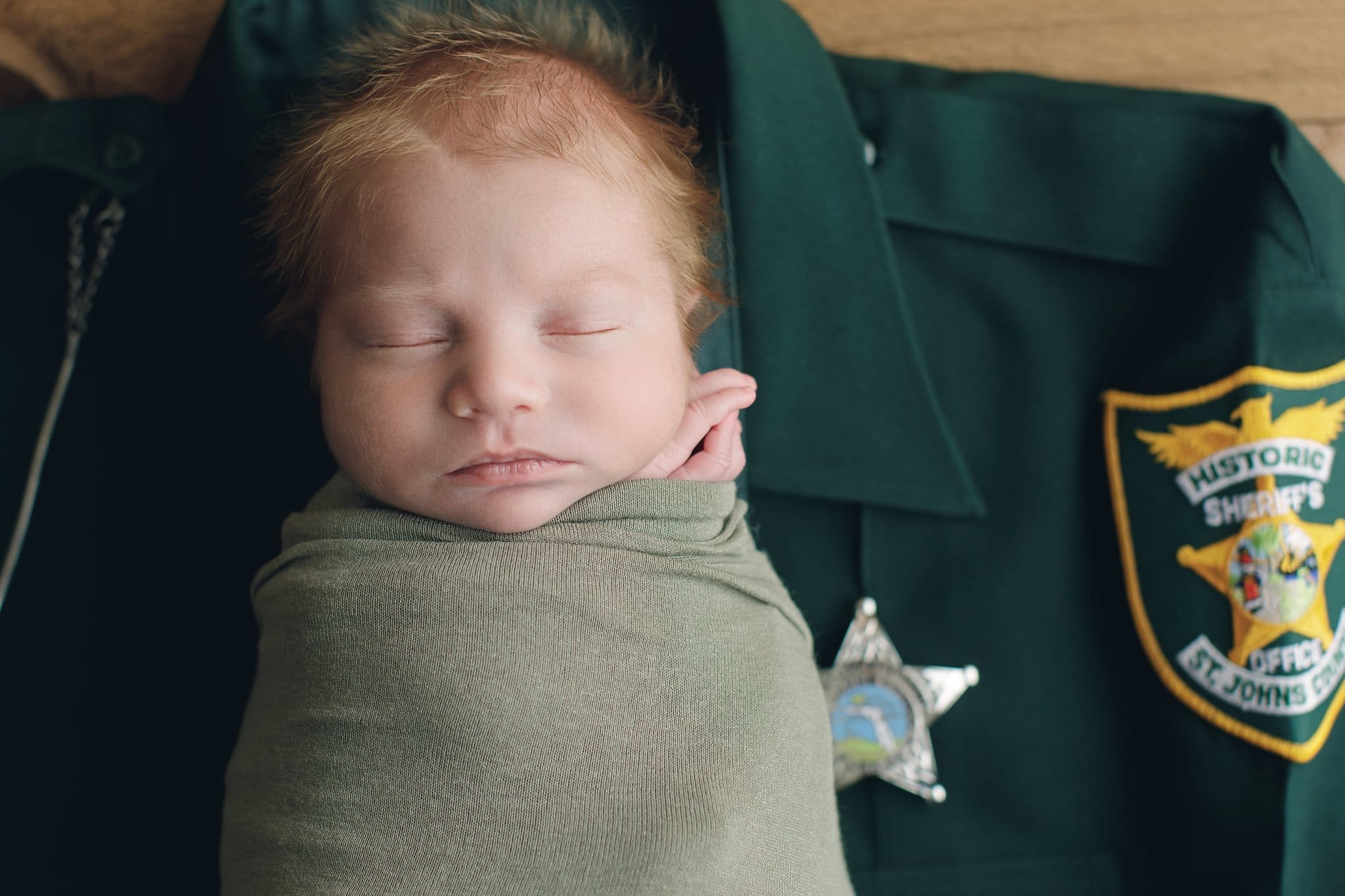 St Johns County Newborn Photographer baby boy with fuzzy hair swaddled and on top of daddy's uniform