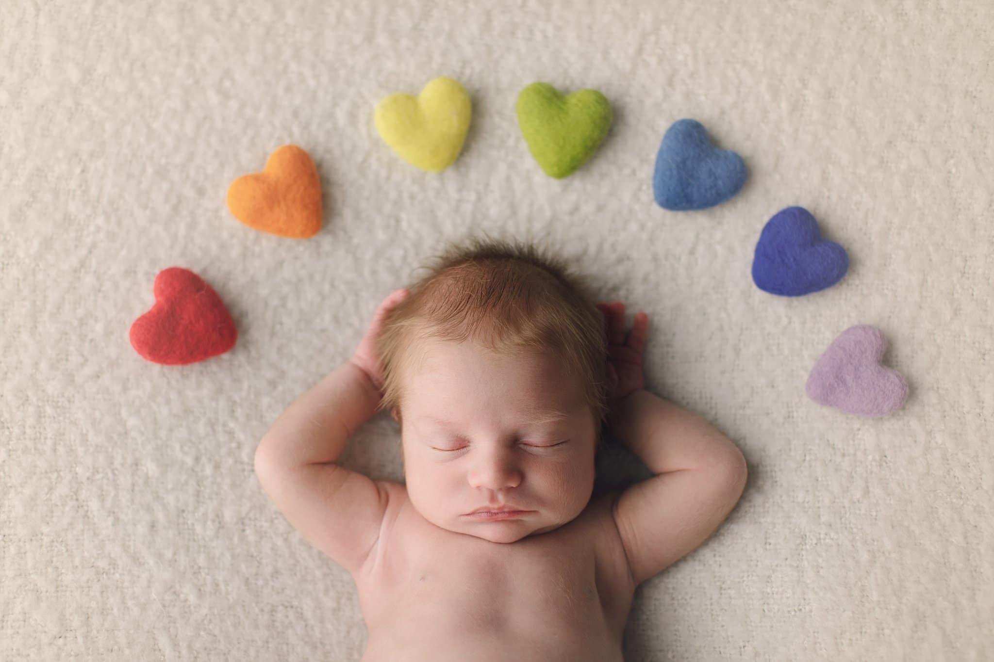 St Johns County Newborn Photographer baby boy with fuzzy hair rainbow baby sleeping on cream blanket with multicolored hearts making a rainbow