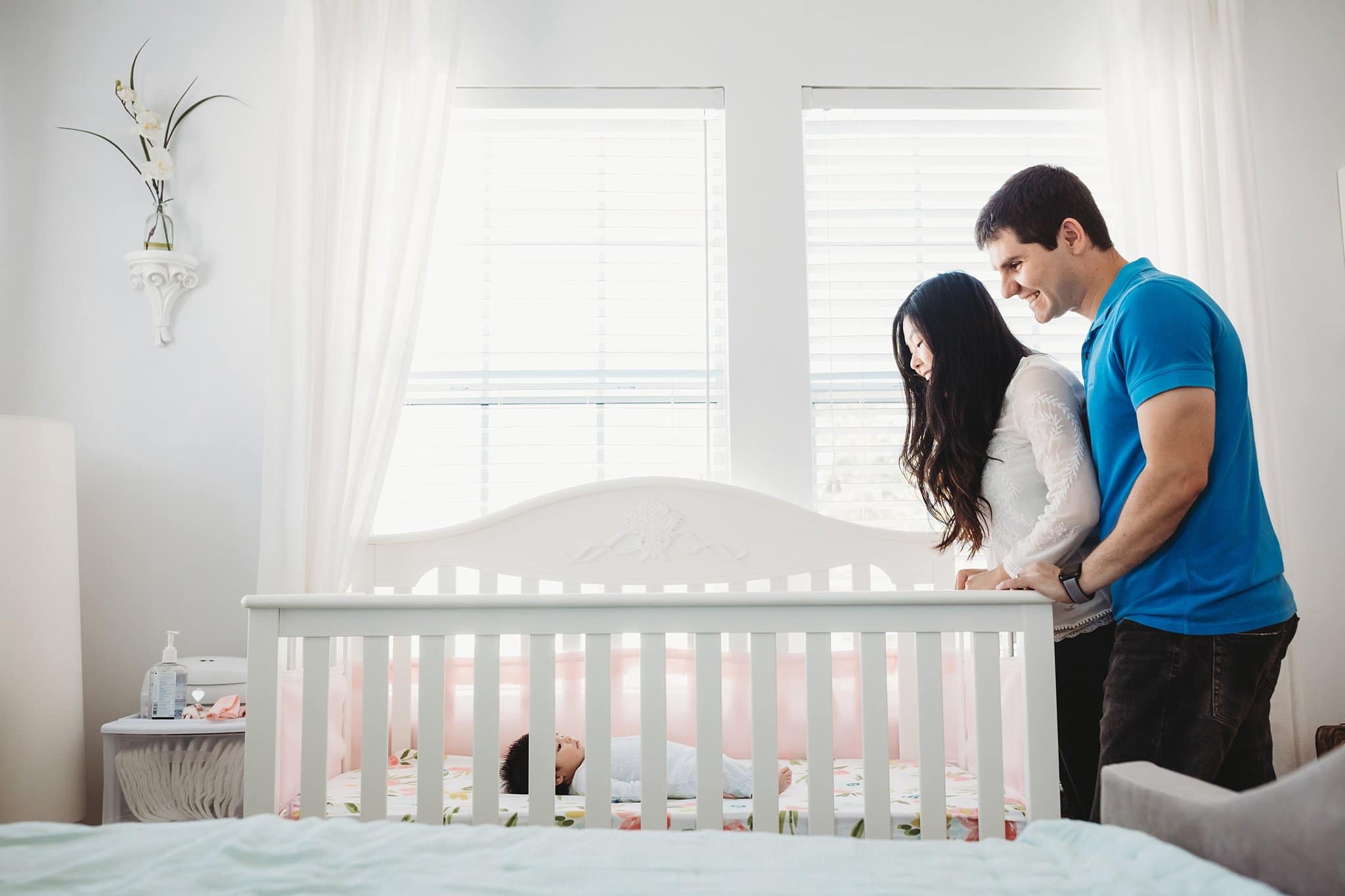 Jacksonville Photographer in home lifestyle newborn photography session mom and dad lookign at newborn baby girl in white crib with beautiful window light flowing in