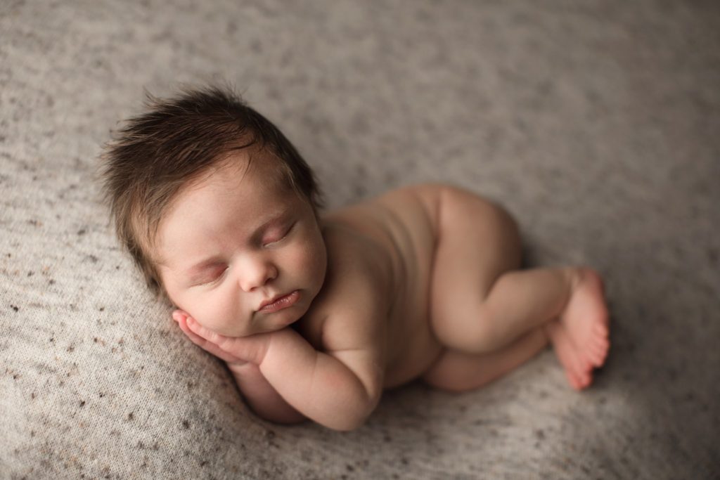 newborn baby boy with fuzzy hair sleeping on speckled cream and beige backdrop sidellying pose