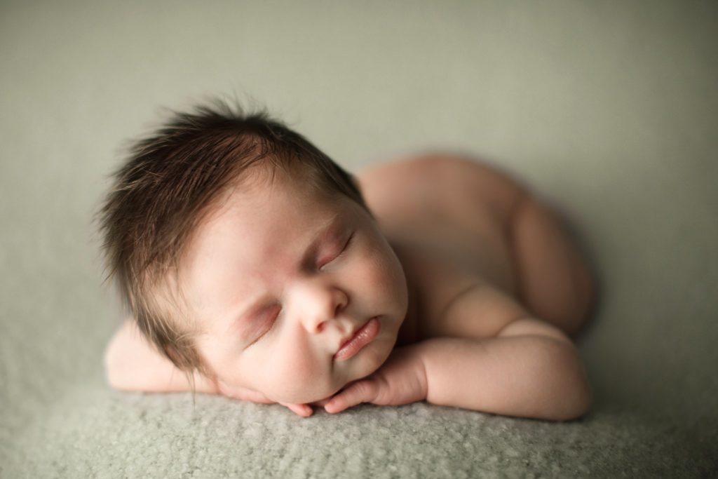 newborn baby boy with fuzzy hair sleeping on mint green backdrop forward facing pose