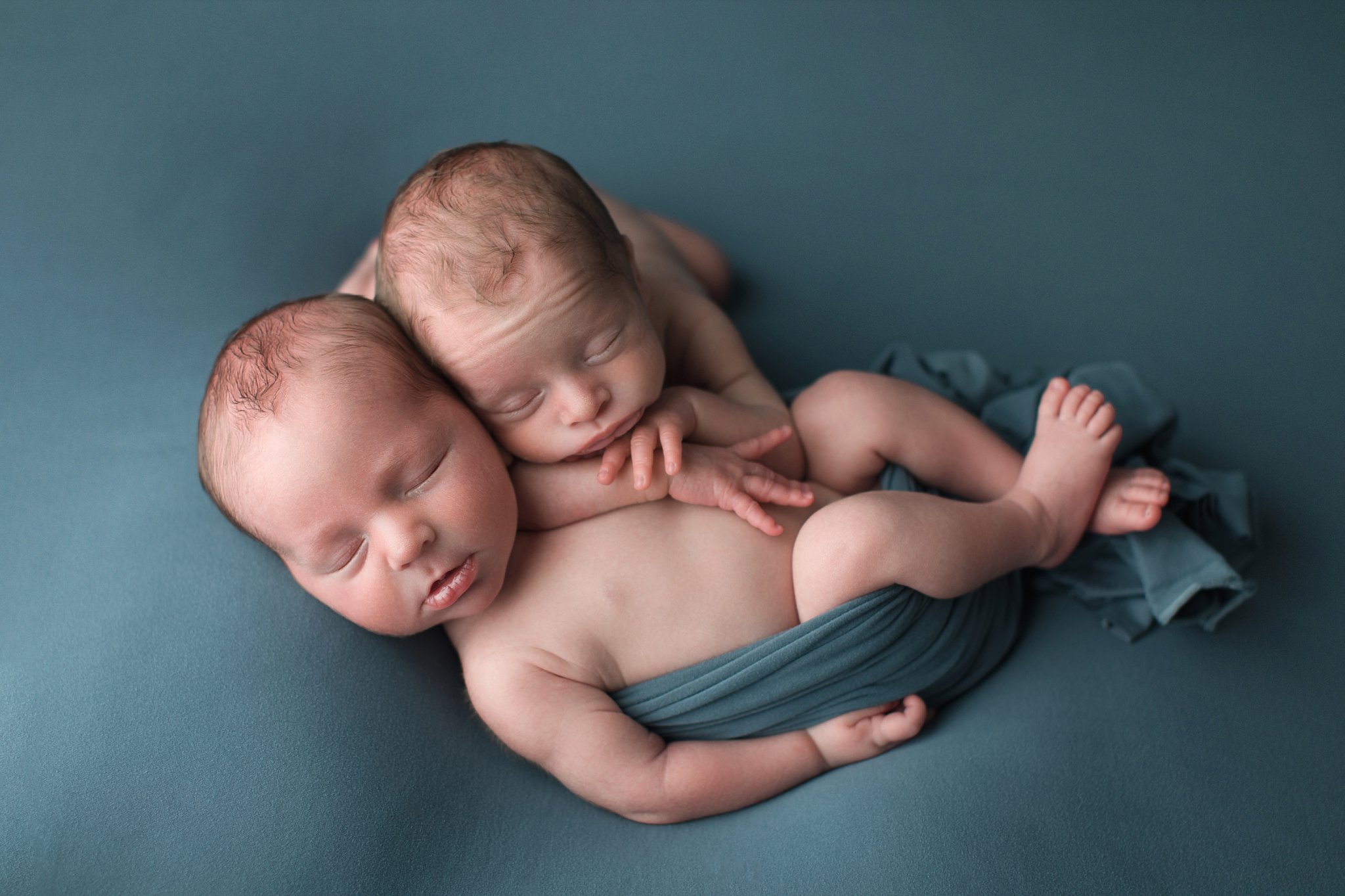 newborn baby boys snuggled and sleeping on teal blanket