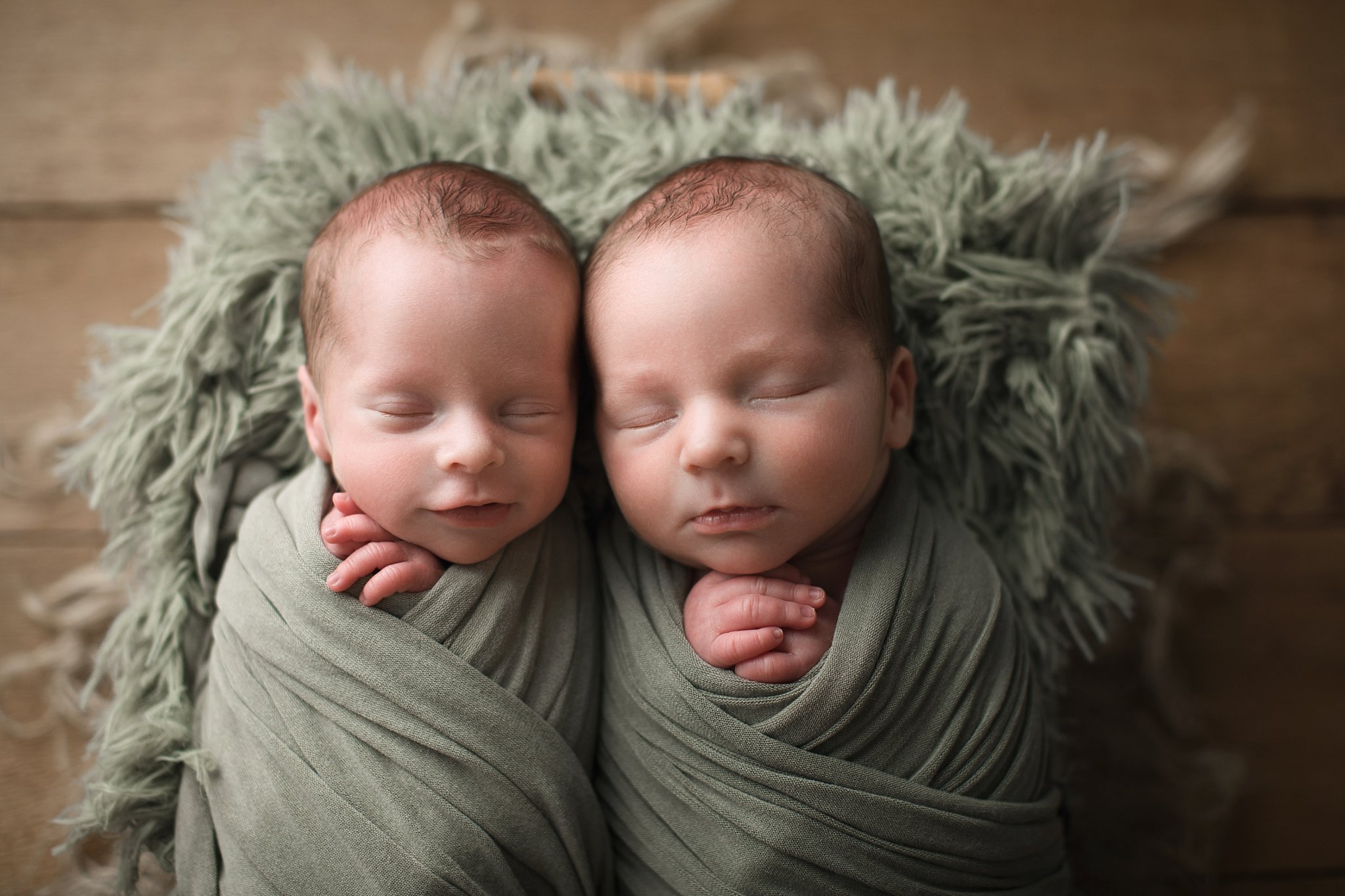 newborn twin baby bous swaddled and sleeping on sage green fur