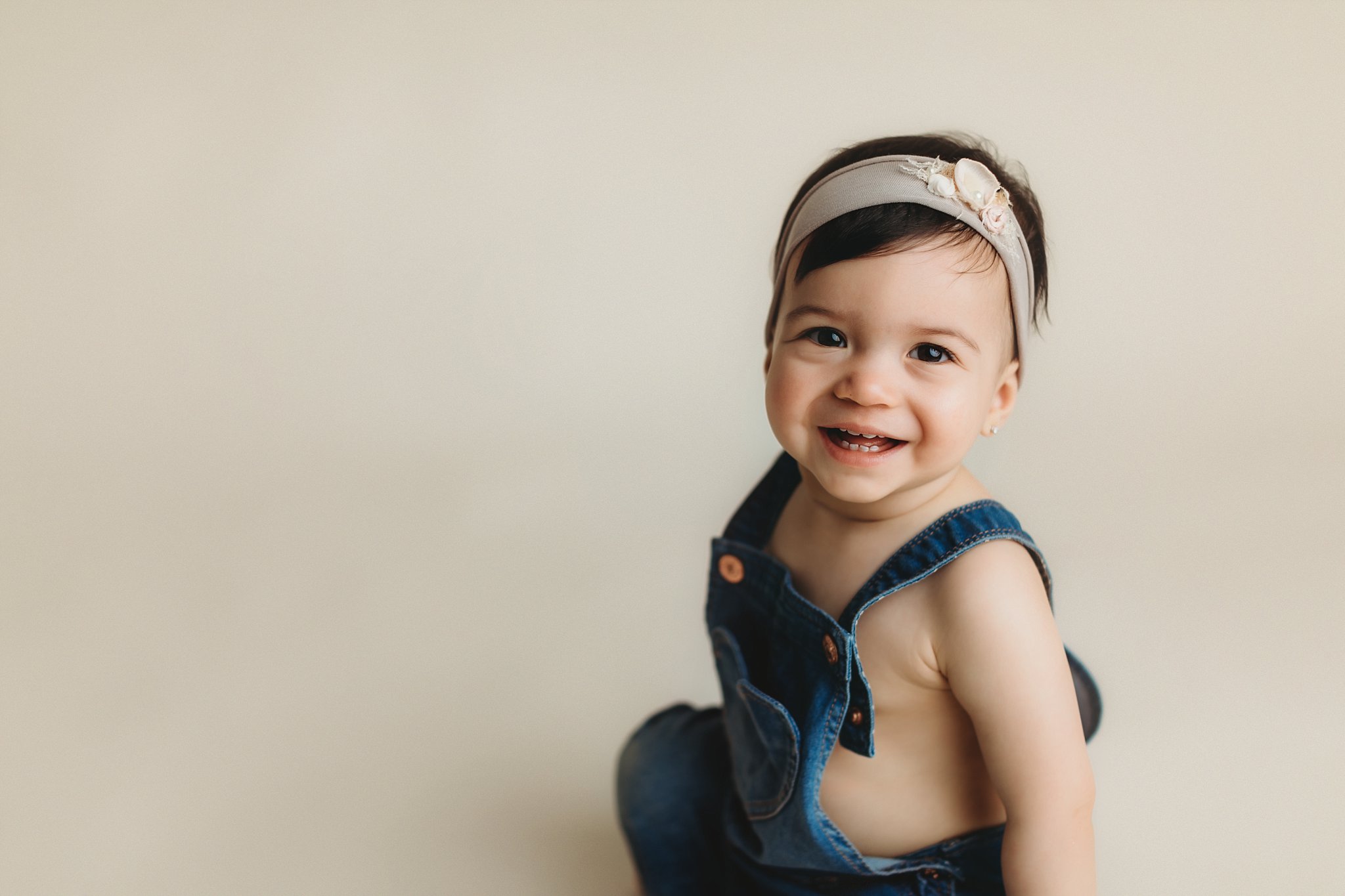 Children's Photo Studio in Jacksonville 1 year old little girl on cream seamless background in denim overalls and pretty headband