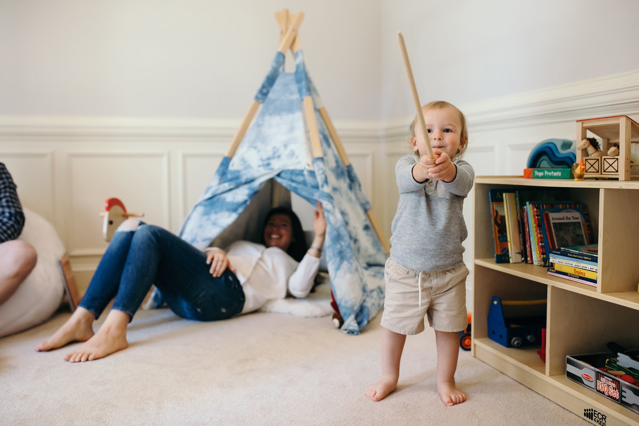 toddler boy playing with a stick in playroom with blue teepee in background