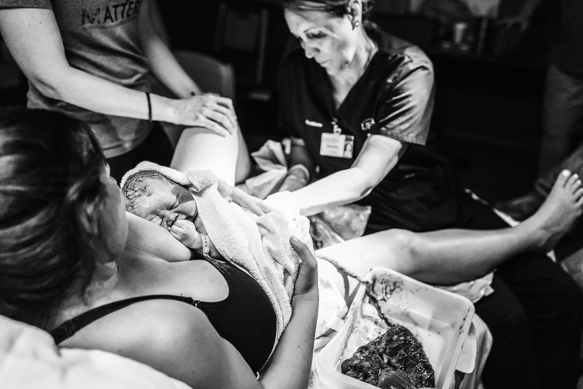 Natural Birth Photography black and white image mom holding newborn baby. midwife and placenta in background