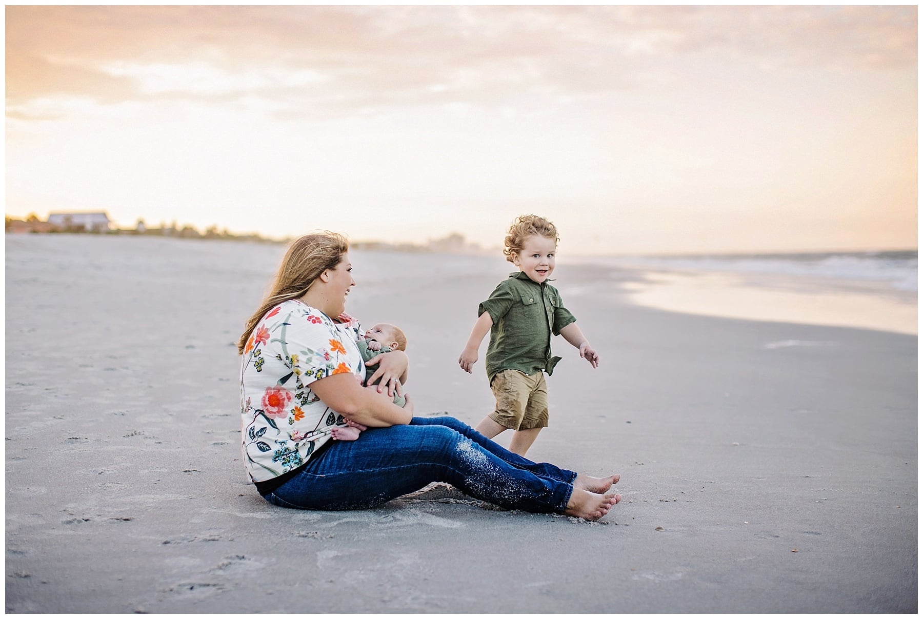 mom holding 2 month old son while toddler runs around on the beach in ponte vedre florida