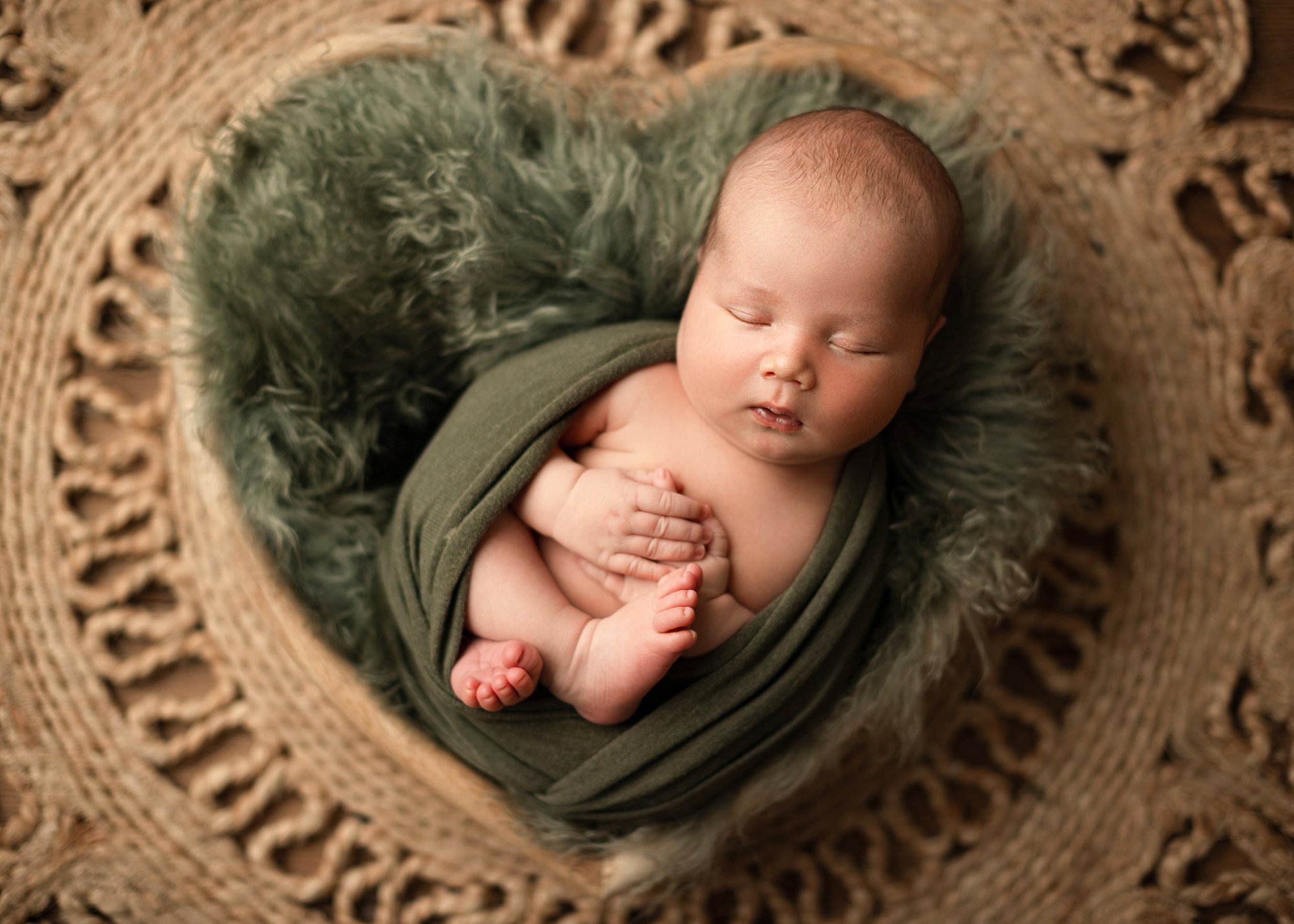 newborn baby in heart basket with green fur