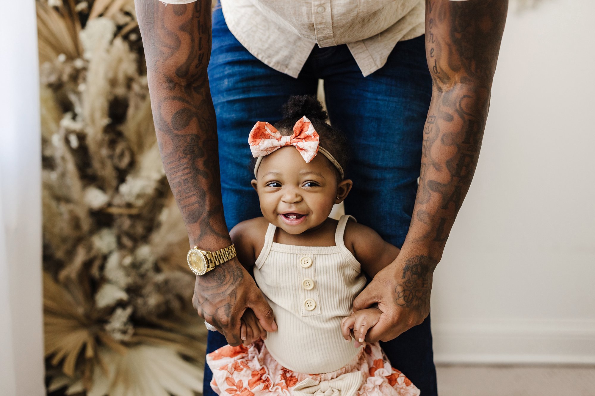 dad with tattoos helping infant daughter stand