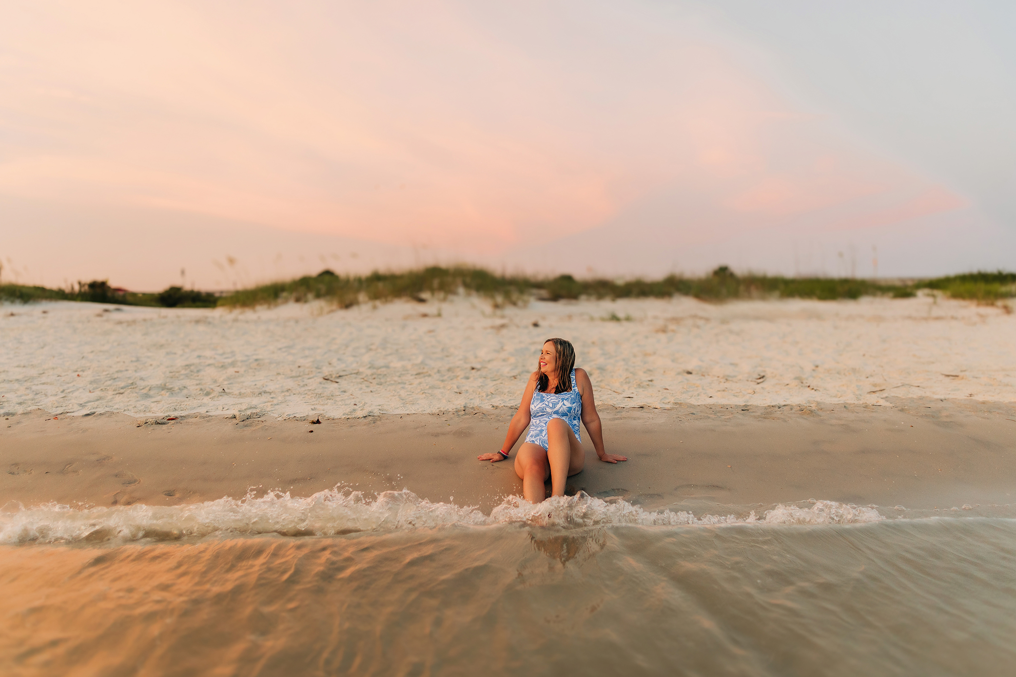 Breast cancer survivor and mother sitting at the shoreline during her family photography session