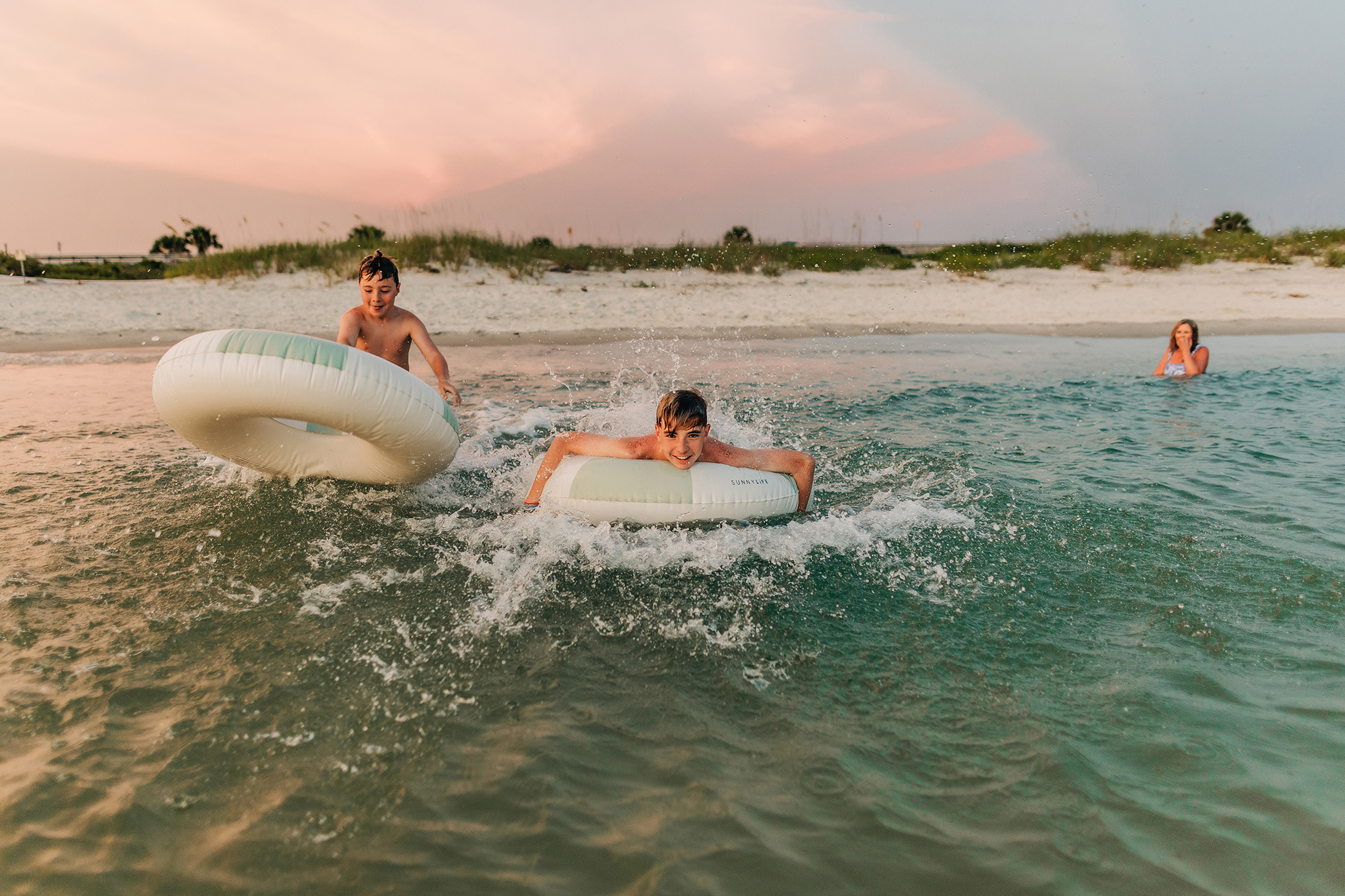 Two brothers splashing and playing on floats during a candid family beach session
