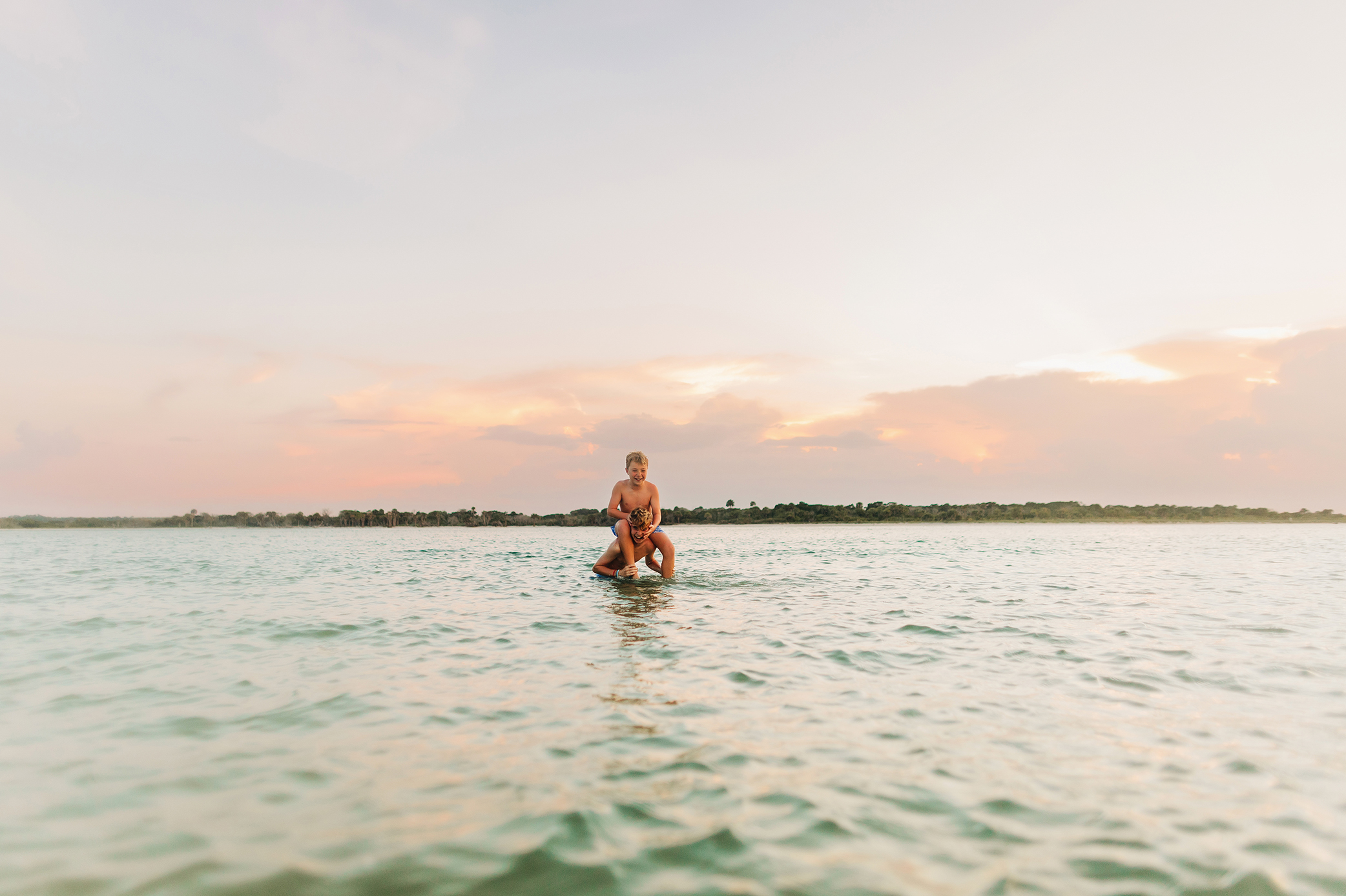 Two brothers playing together in the water beneath a pastel sunset sky