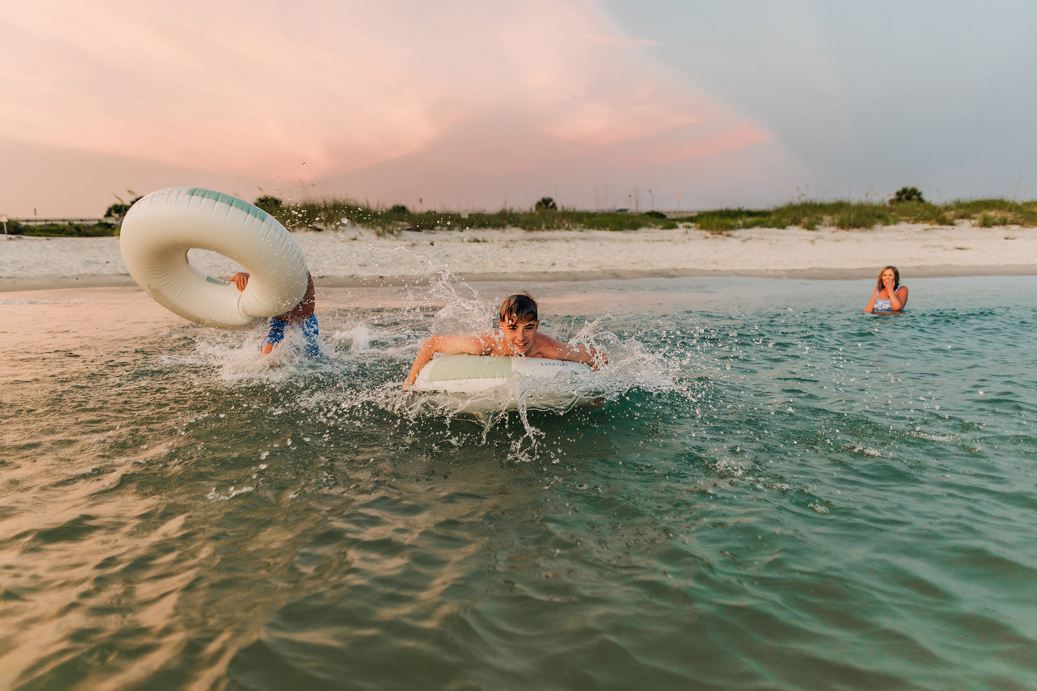 Photography Two brothers racing through the shallow water on inflatable floats while their mother watches