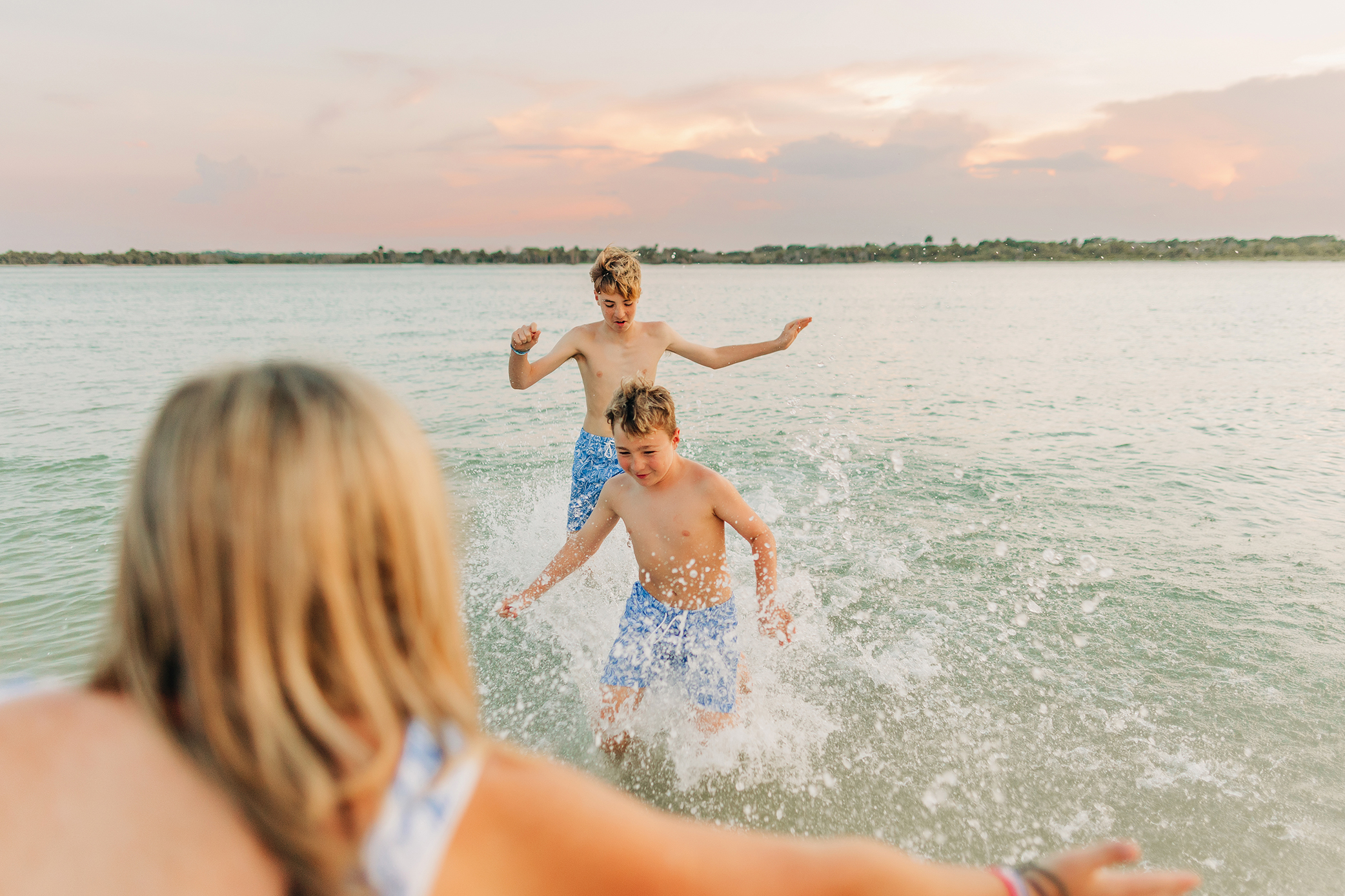 Mother watching her two sons run and splash toward her in the water