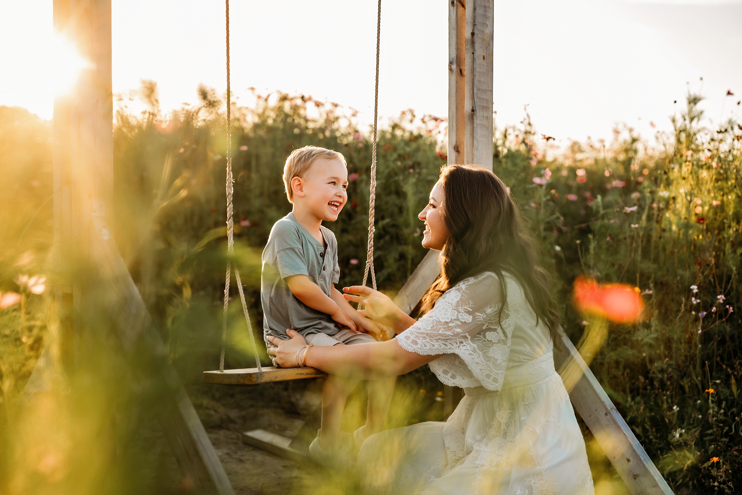 Mother and young son laughing together on the wooden swing at Parker Flower Farms during golden hour.