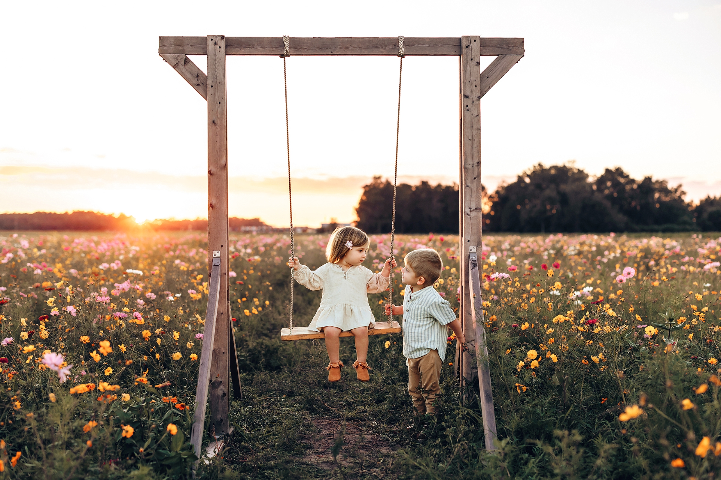 Young siblings sharing a quiet moment on the wooden swing surrounded by wildflowers at Parker Flower Farms.